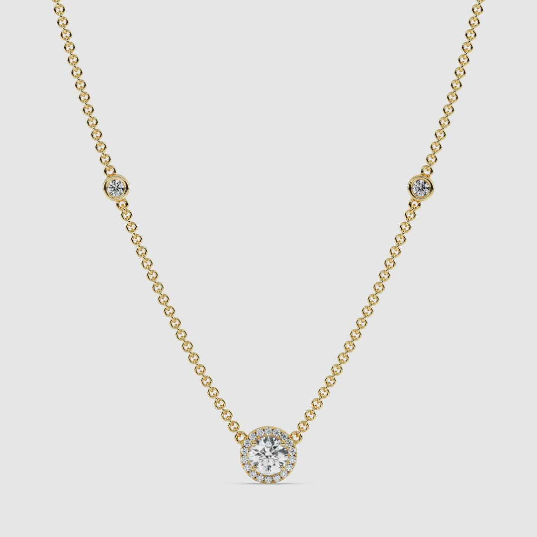Close-up video of an 18K yellow gold Round Diamond Accent Halo Bezel Station Necklace featuring a 1.00ct IGI Certified round lab-grown diamond at the center, surrounded by a halo of smaller EF/VS diamonds. The necklace chain is adorned with bezel-set diamonds, showcasing its exquisite craftsmanship and radiant golden hue.