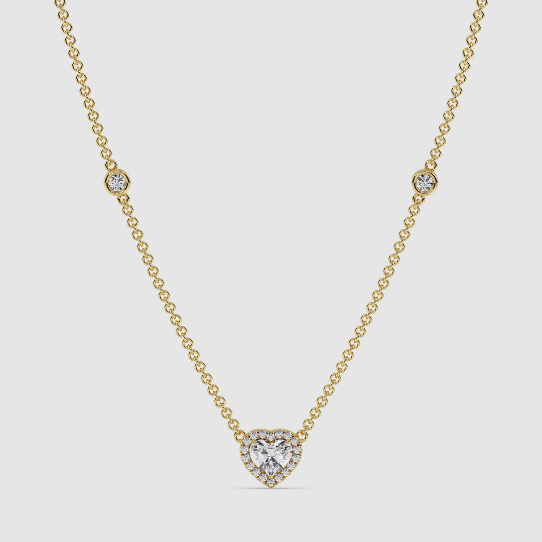 video of the Elegant Heart Diamond Accent Halo & Bezel Station Necklace in 18K Yellow Gold. The central 1.00ct heart-cut lab-grown diamond sparkles brilliantly, surrounded by a halo of smaller EF/VS diamonds. The yellow gold chain features bezel-set round diamonds, enhancing the necklace’s luxurious and radiant appeal. The piece is displayed against a neutral background to showcase its intricate craftsmanship and timeless elegance.
