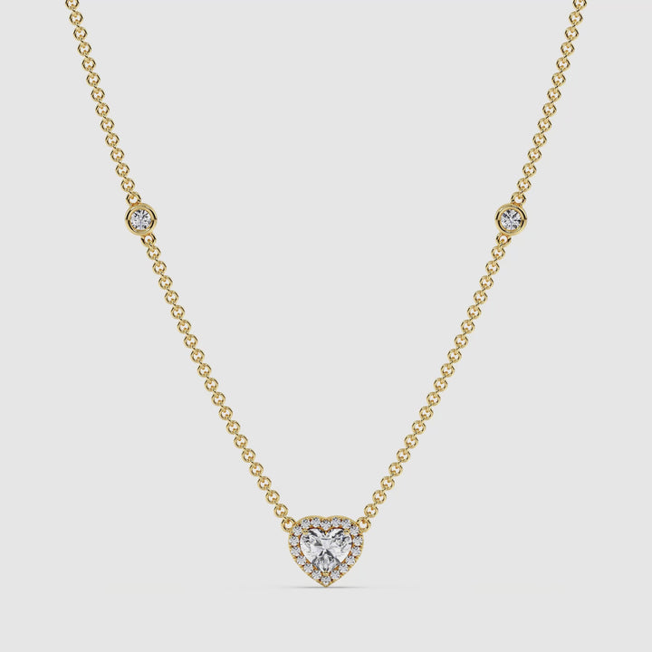 video of the Elegant Heart Diamond Accent Halo & Bezel Station Necklace in 18K Yellow Gold. The central 1.00ct heart-cut lab-grown diamond sparkles brilliantly, surrounded by a halo of smaller EF/VS diamonds. The yellow gold chain features bezel-set round diamonds, enhancing the necklace’s luxurious and radiant appeal. The piece is displayed against a neutral background to showcase its intricate craftsmanship and timeless elegance.